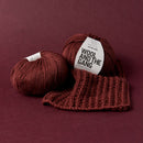 Two balls of brown yarn with a knitted item and 'Wool and the Gang' label on a maroon background.