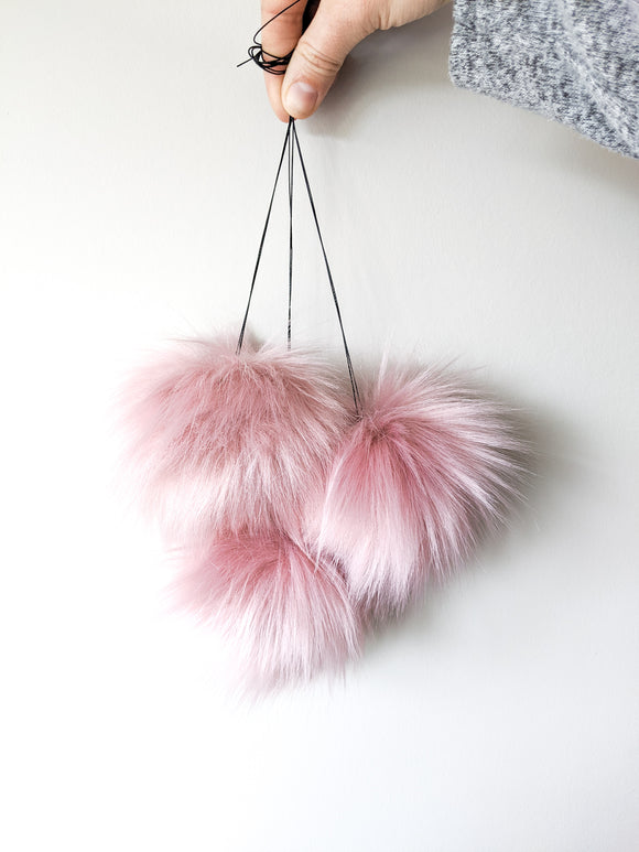 Rose blush faux fur pom poms held by strings.
